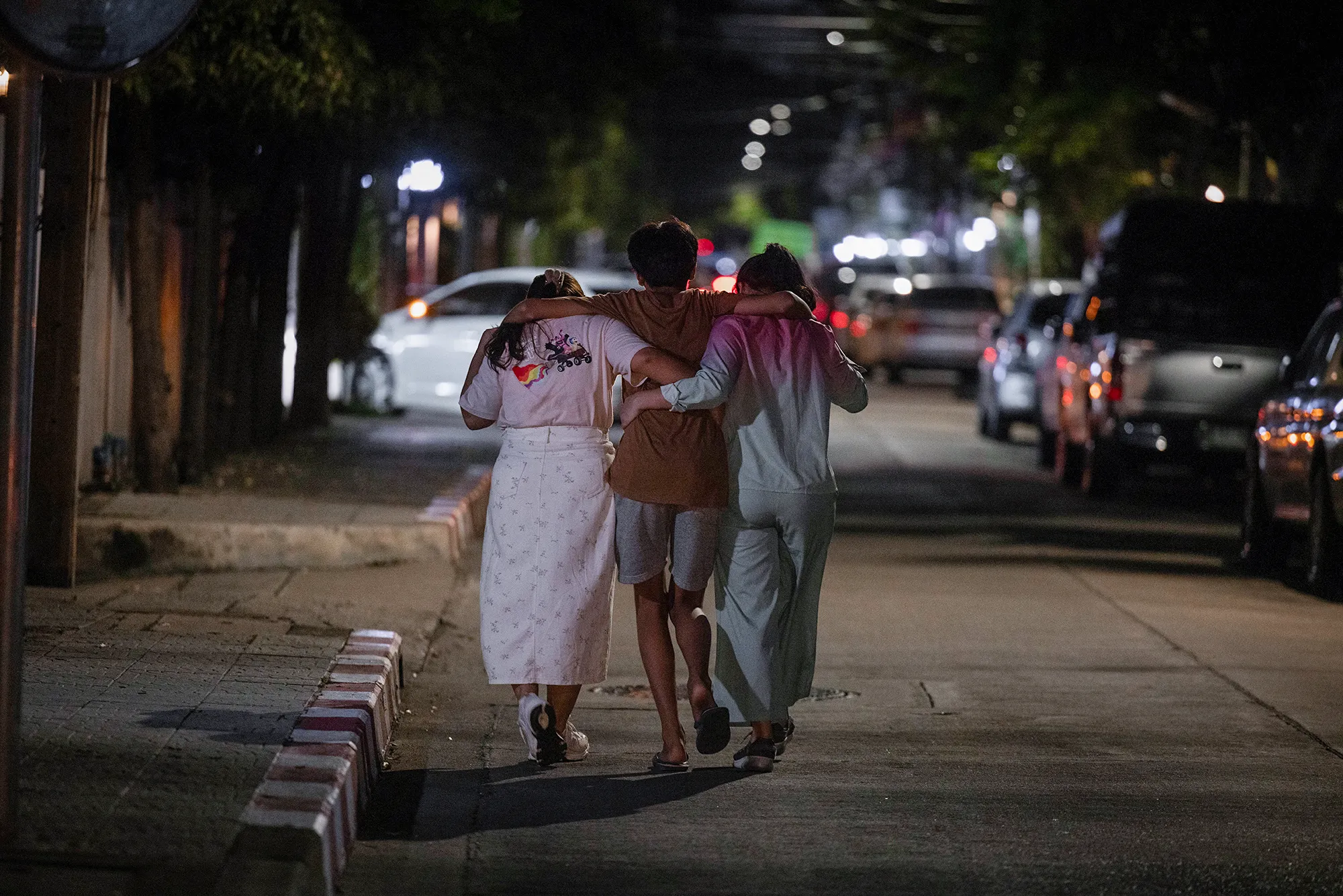 A dark street corner with 2 women helping a man walk down the street